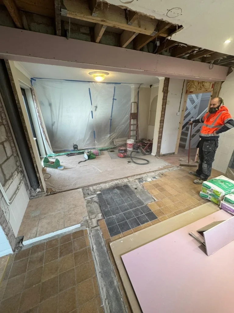 Construction site inside a house with a worker in high-vis and bags of plaster.