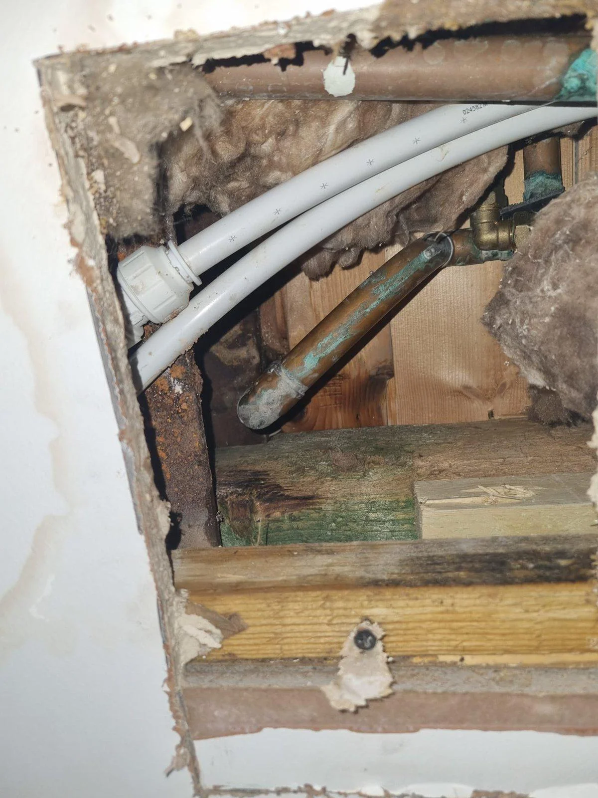 Failed 22mm copper pipe in a ceiling void with green corrosion staining at the point of failure