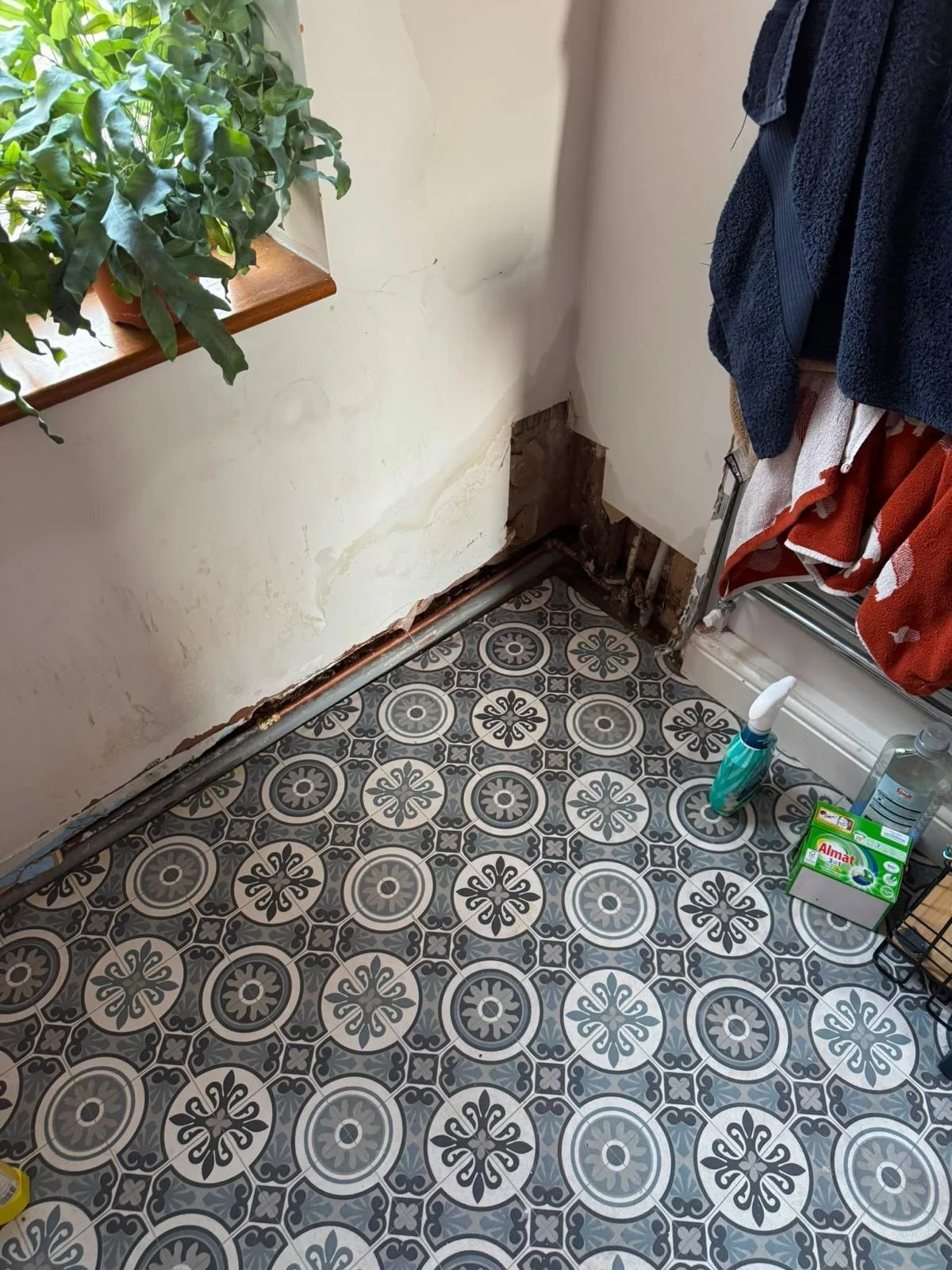 Hallway with a water-stained wall, plaster removed at low level and copper pipework exposed during an emergency plumbing repair in Flintshire