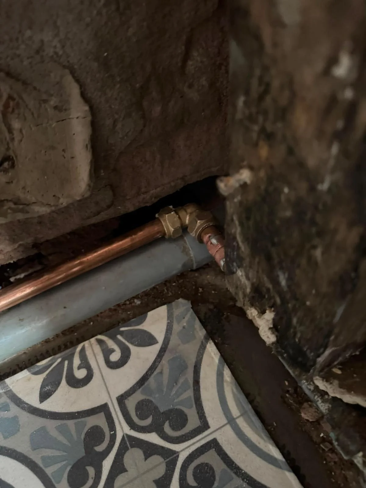 Brass compression elbow joining new copper pipe around a corner at the base of a wall