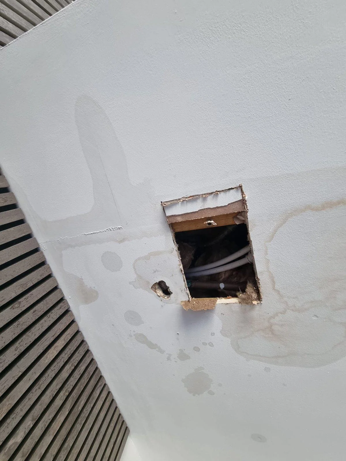 Ground floor ceiling in a Wirral house with water staining and an opening cut to trace a leak, pipework visible in the void above