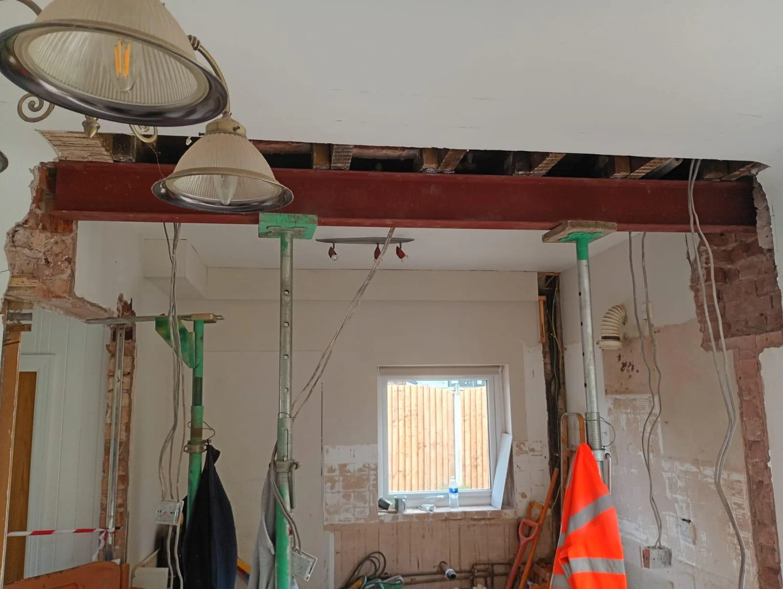 Red steel beam installed across an opening in a residential interior with metal support props.