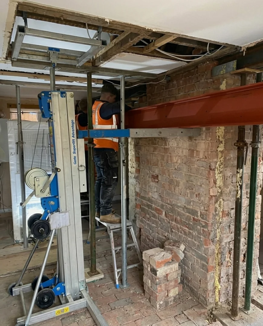 Using a Genie lift to position a structural steel beam into a brick wall opening during renovation.