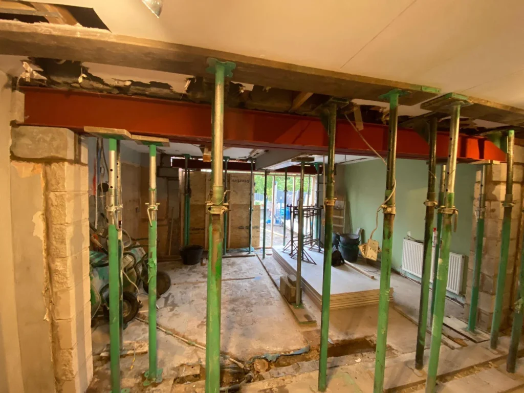 Temporary steel prop supports installed during load-bearing wall removal for structural alteration.