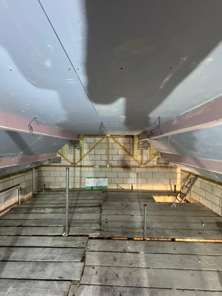 Loft space with newly installed plasterboard ceiling and exposed timber framework.