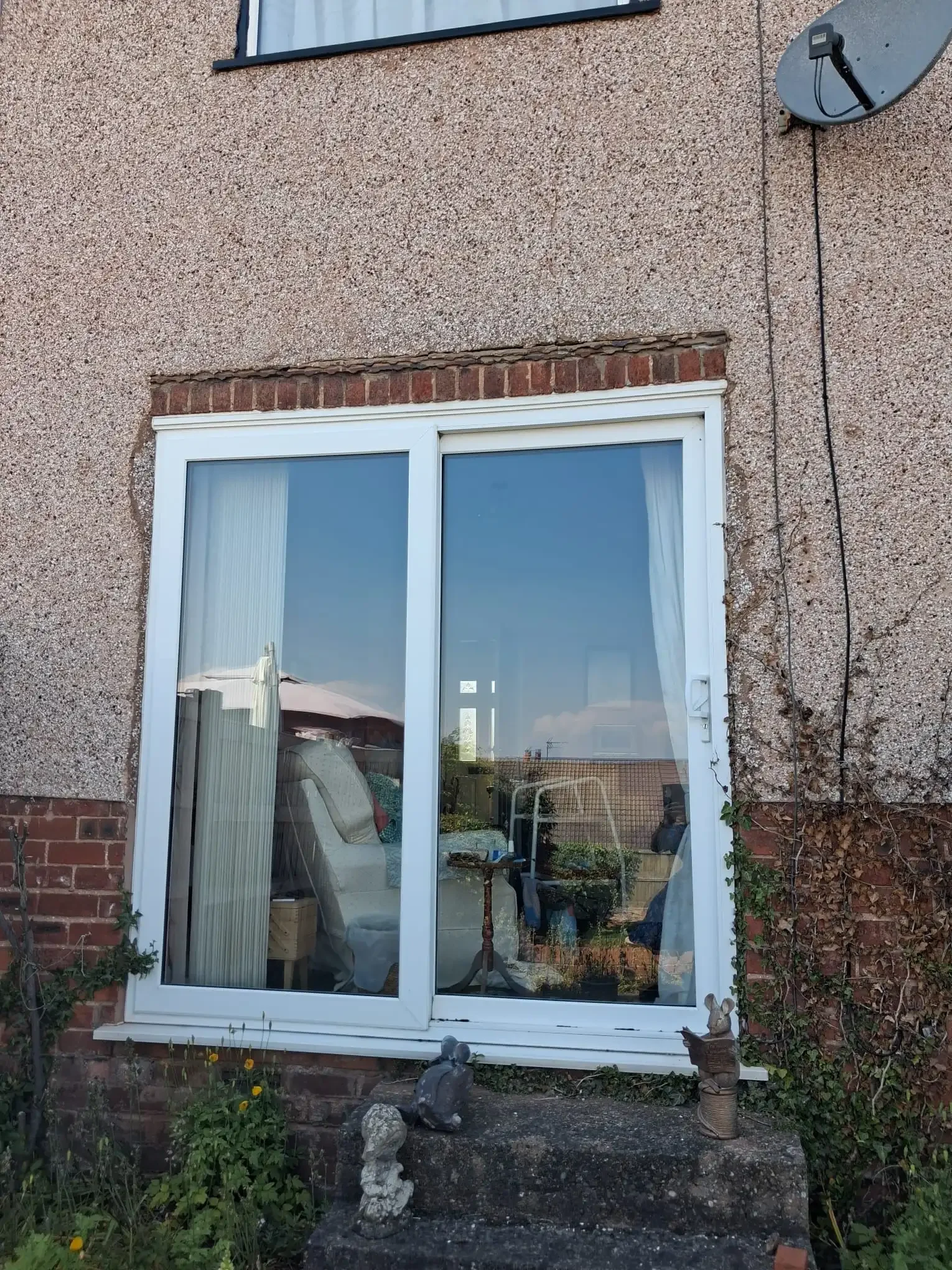 White uPVC patio doors in a pebble-dashed rear wall, with a course of exposed brickwork over the frame