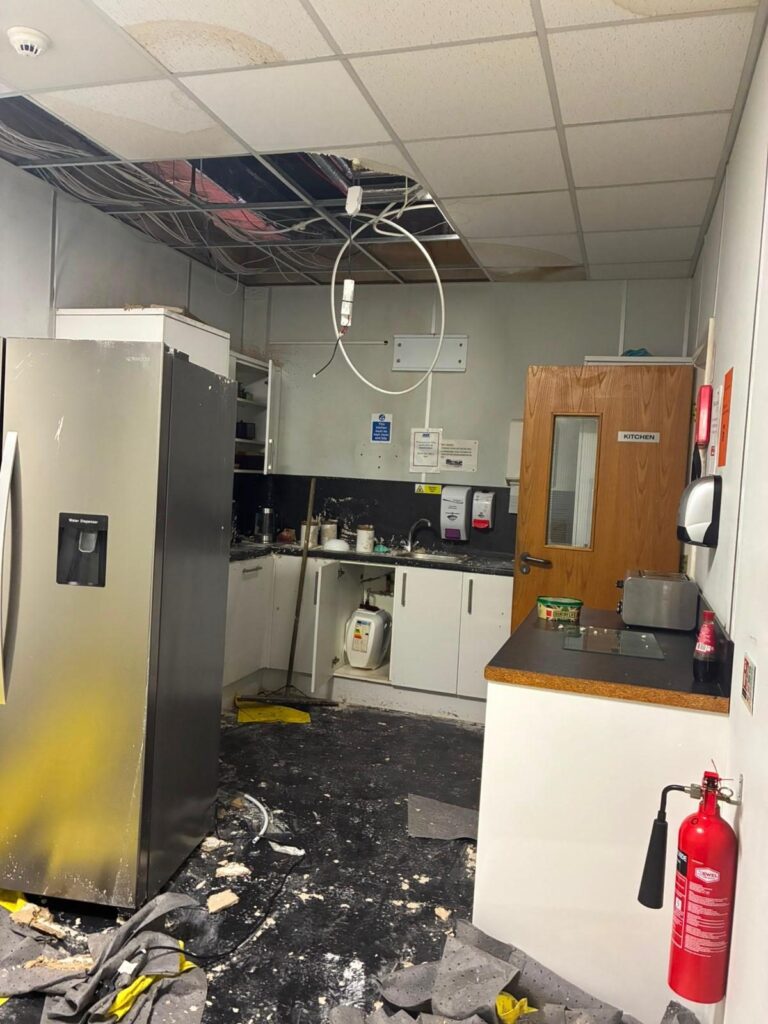Commercial kitchen after a burst pipe, with suspended ceiling tiles removed and debris across the floor