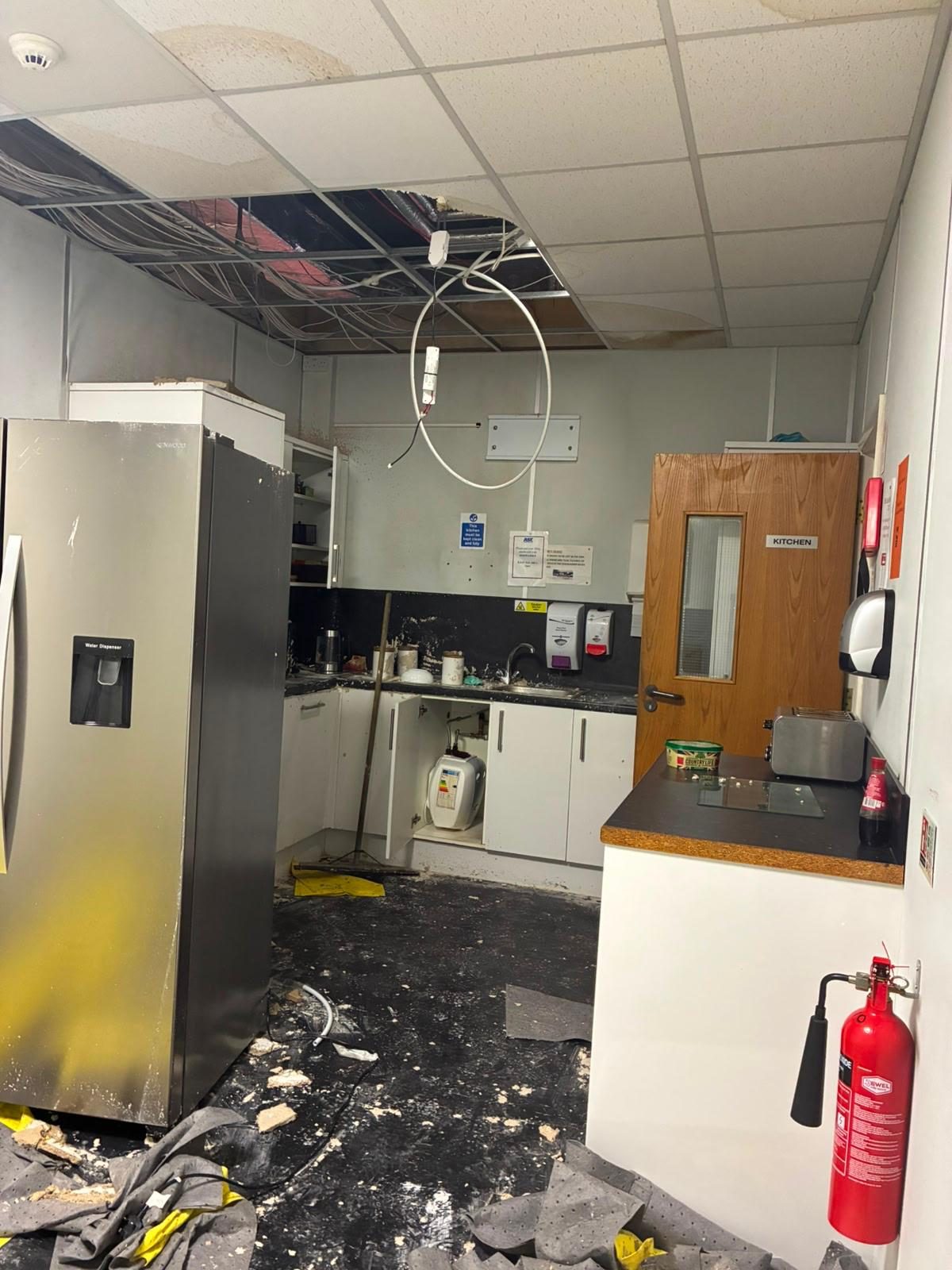 Commercial kitchen after a burst pipe, with suspended ceiling tiles removed and debris across the floor