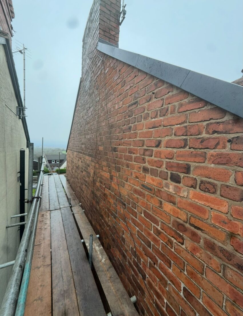 Scaffolded gable elevation before repointing, showing eroded mortar joints and earlier cement repairs