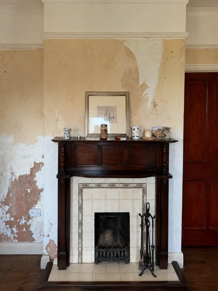 Damp affected walls and peeling decoration around a fireplace before treatment in Hope, flintshire