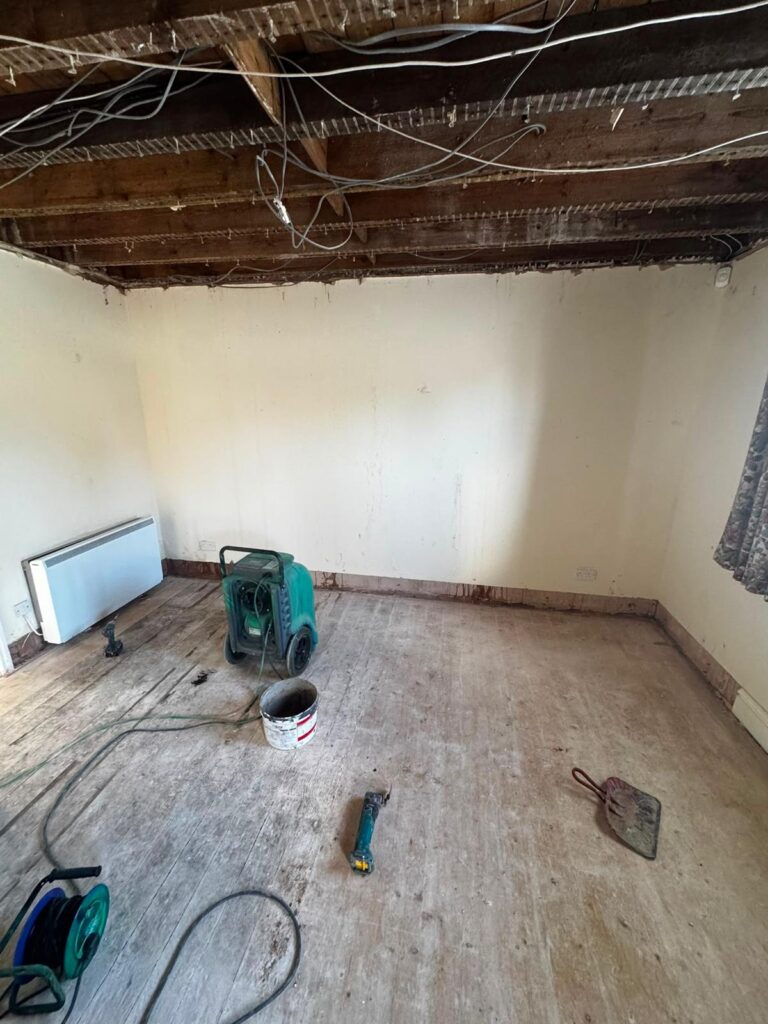Room stripped back to bare floorboards with a heater and dehumidifier running to dry the structure after a flood