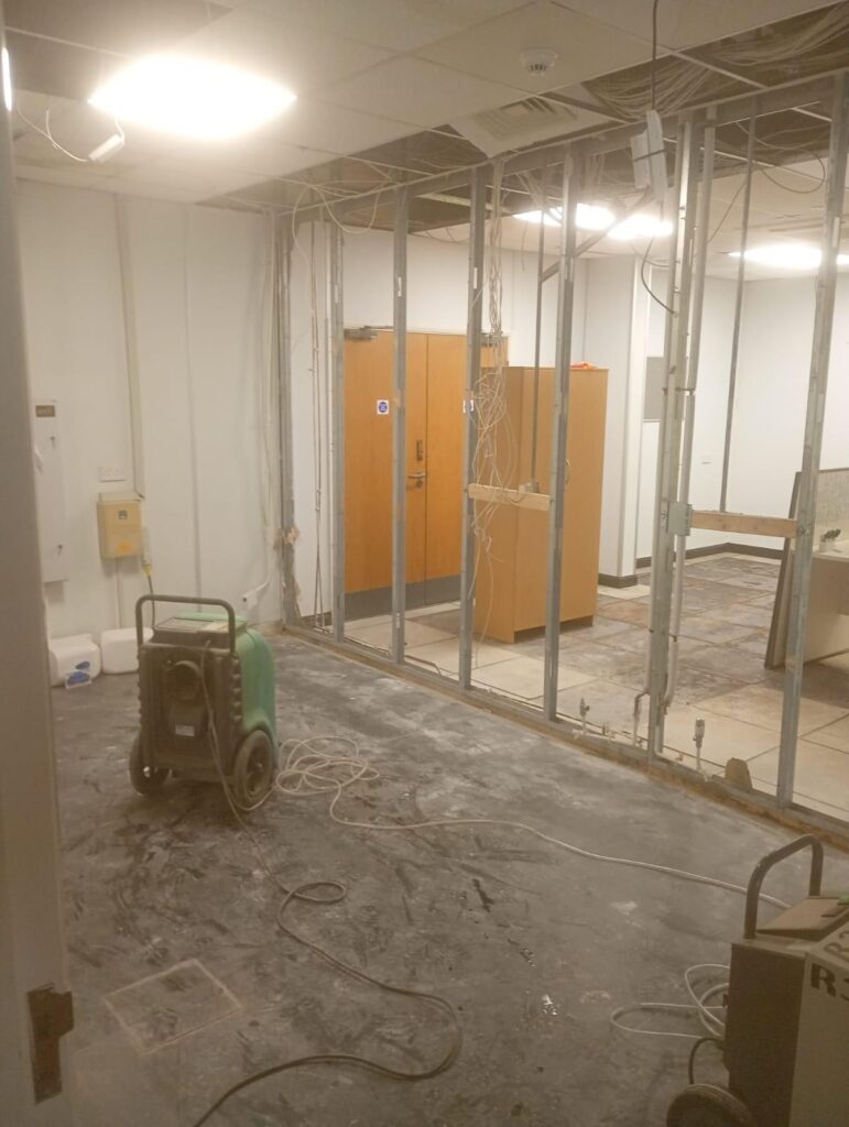 Commercial interior stripped back to metal stud partitions with a dehumidifier running on the bare floor during flood damage restoration