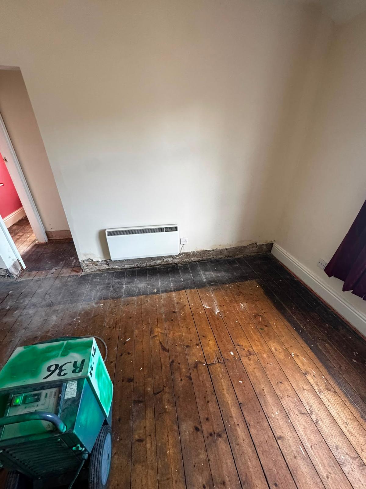 Dehumidifier running on a stripped timber floor during controlled drying after flood damage