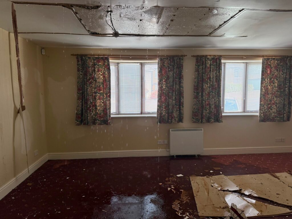 Water-damaged room with a collapsed ceiling and saturated carpet after an internal flood