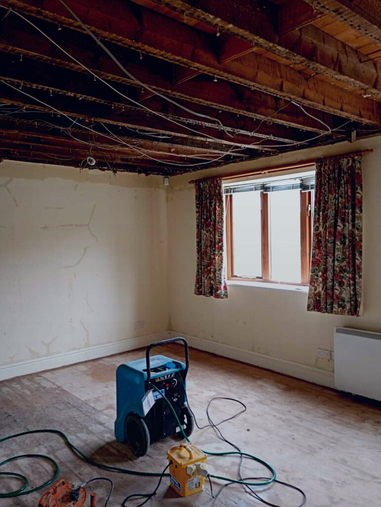 Flood-damaged room stripped out with dehumidifier running during controlled drying