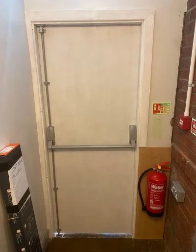 Newly installed FD30 timber fire exit doorset at an industrial unit in Buckley, primed and fitted with a panic bolt before decoration