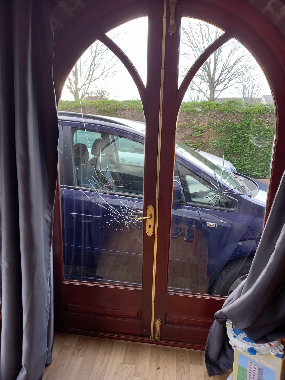 Arched hardwood double doors at a house in Wrexham with the glass cracked in star-shaped fractures after vandalism