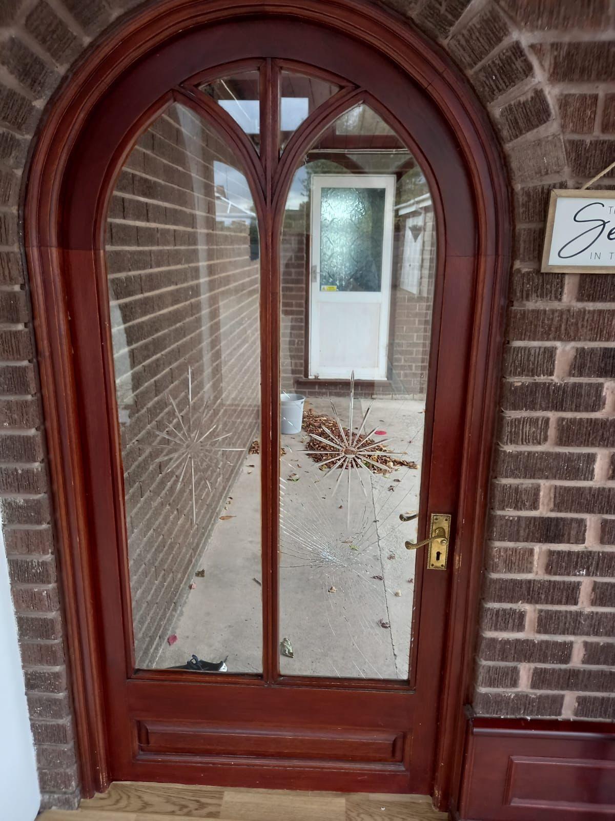 Arched hardwood single door with impact fractures in both glass panes after vandalism