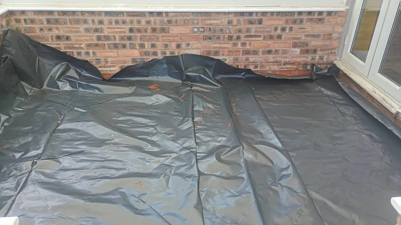 Black damp-proof membrane laid across a garden room floor and turned up at the brick walls