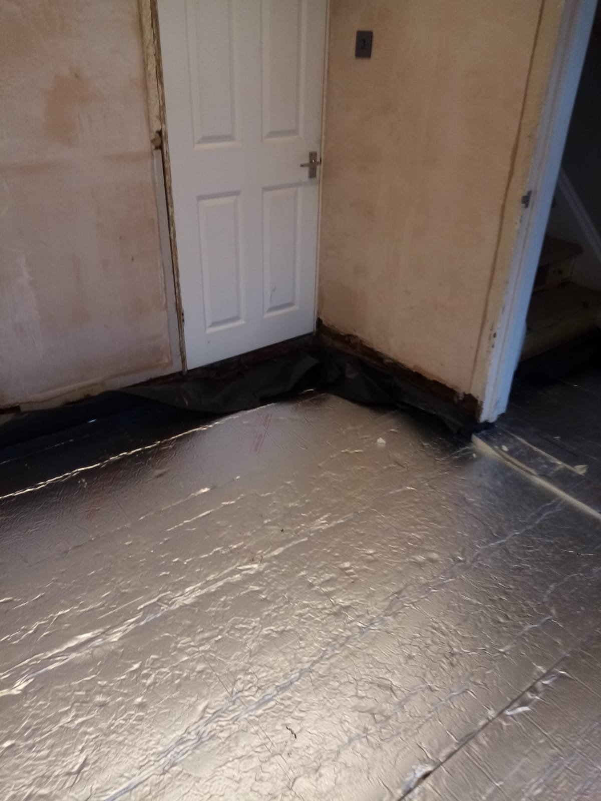 Black damp-proof membrane turned up the base of a plastered wall beside floor insulation boards