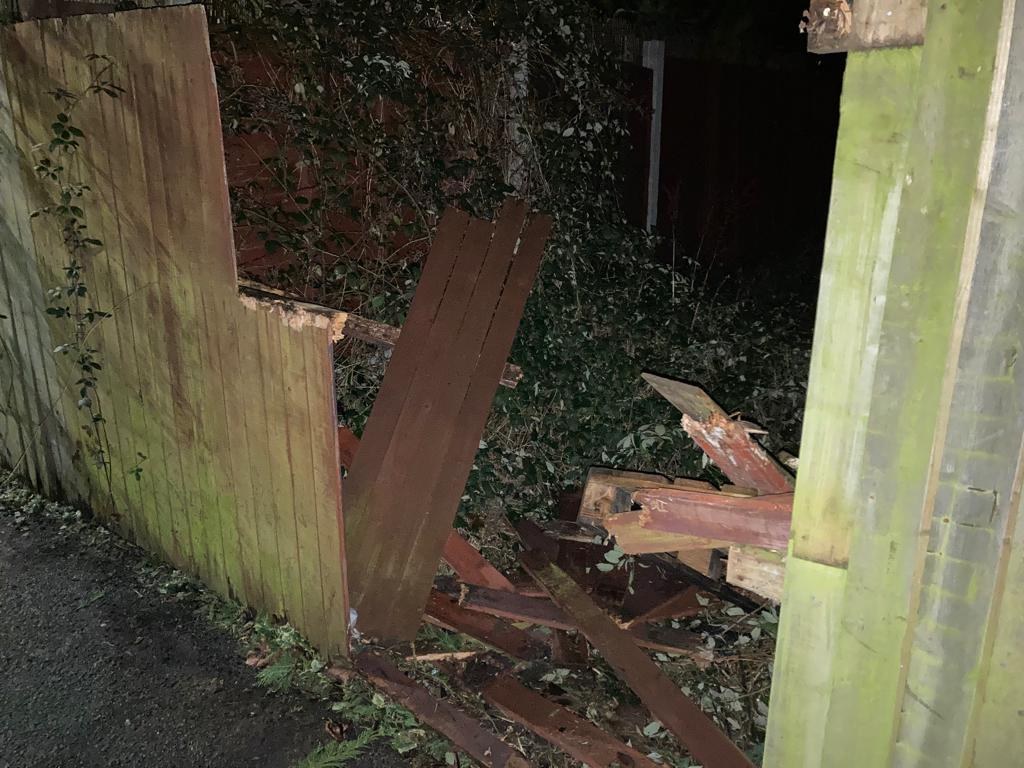 Broken timber fence panel in a garden with the boards splintered and lying on the ground