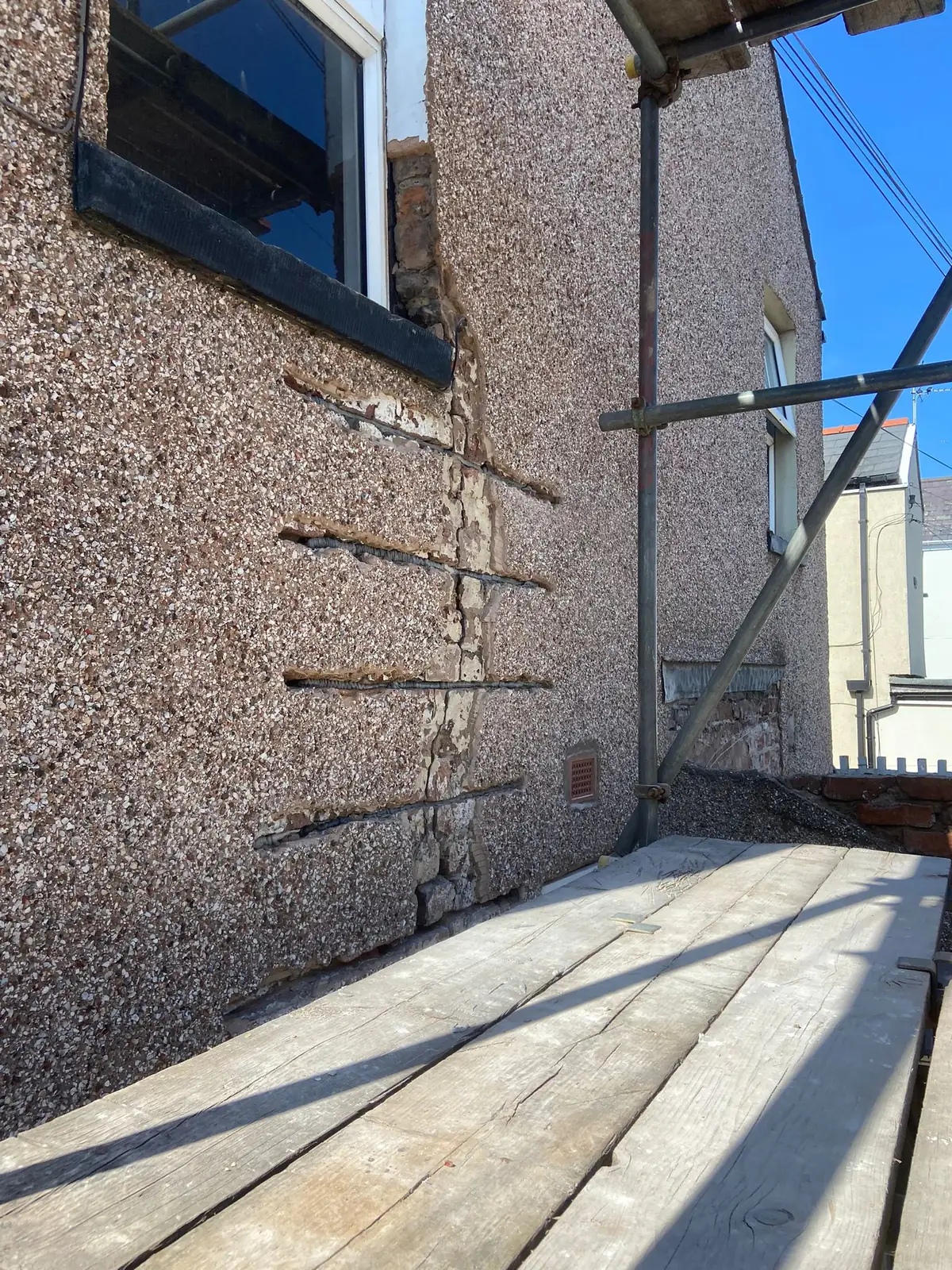 Helical bars set in slots cut across a vertical crack in a pebble-dashed wall, with the render cut back along the crack