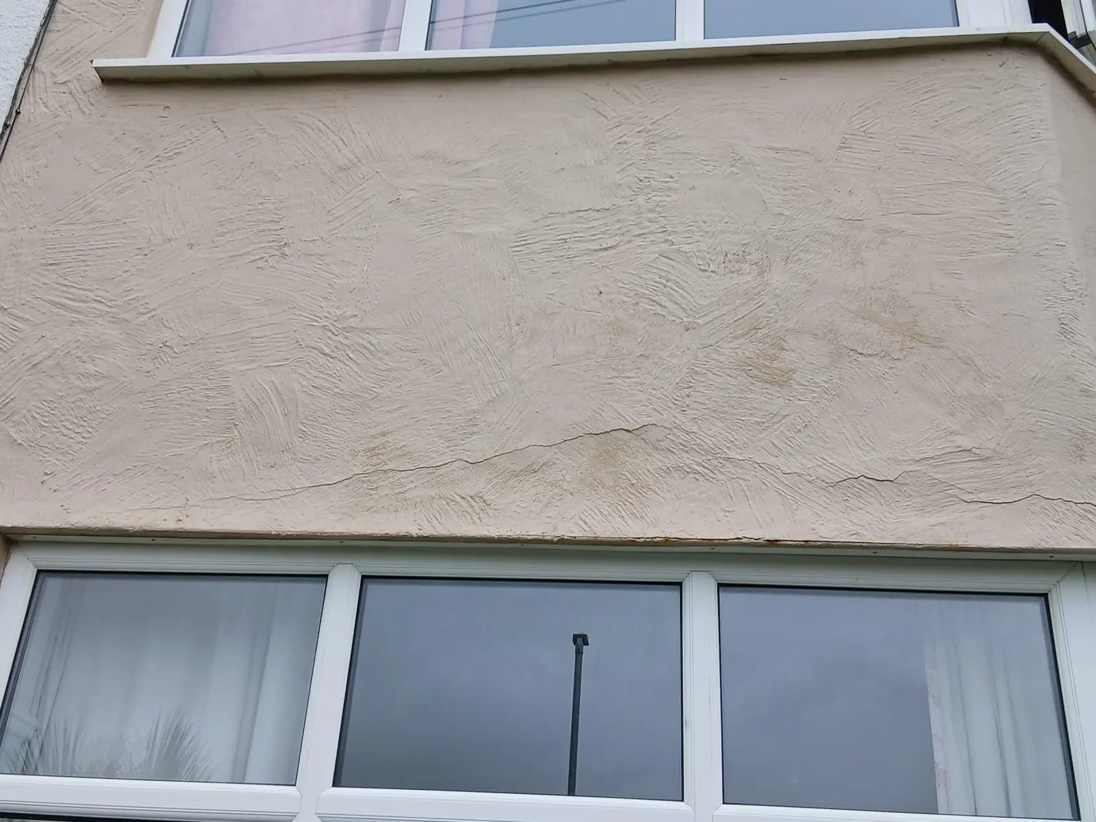Horizontal crack and rust-coloured staining in textured render just above a window