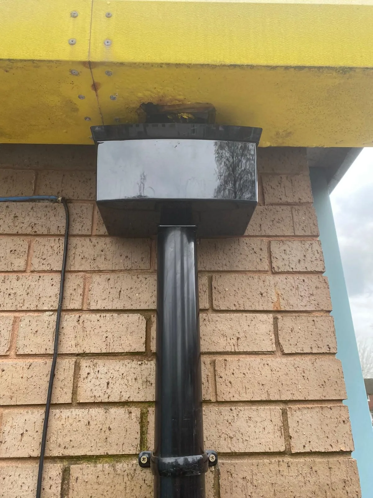 New black uPVC hopper head fitted beneath the painted eaves beam of an industrial unit, with the downpipe running below it