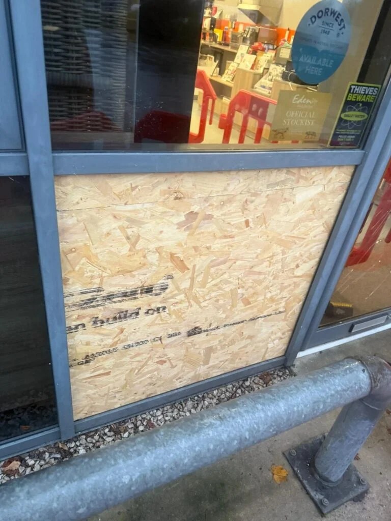Low-level shopfront panel boarded up with OSB sheet fixed inside the aluminium frame after a break-in