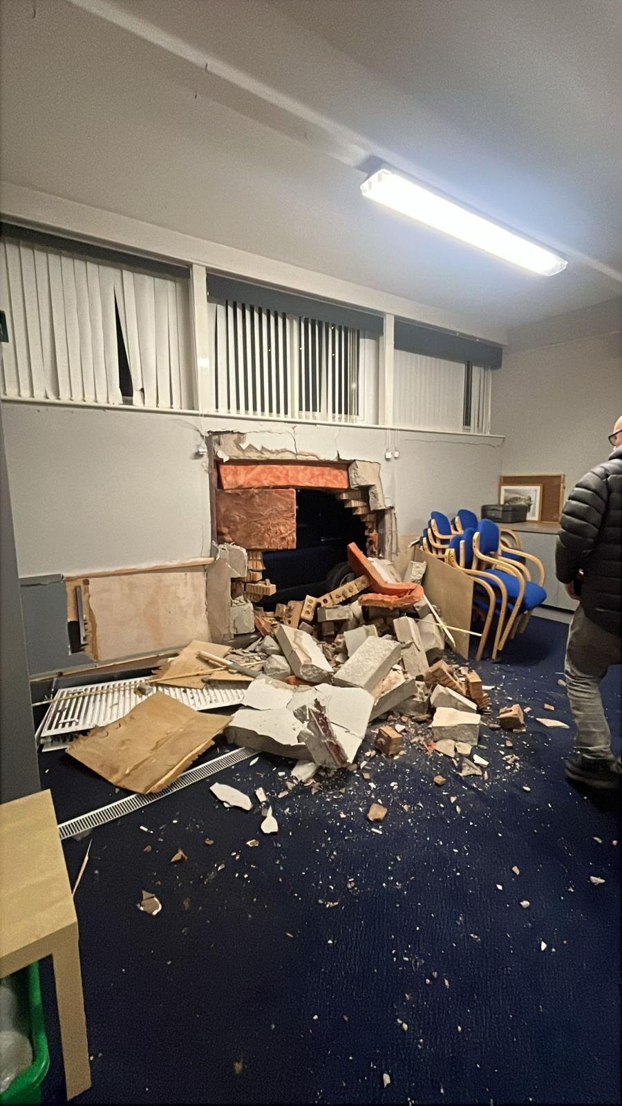 Inside a meeting room after a vehicle hit the outside wall, with rubble, insulation and plaster across the carpet