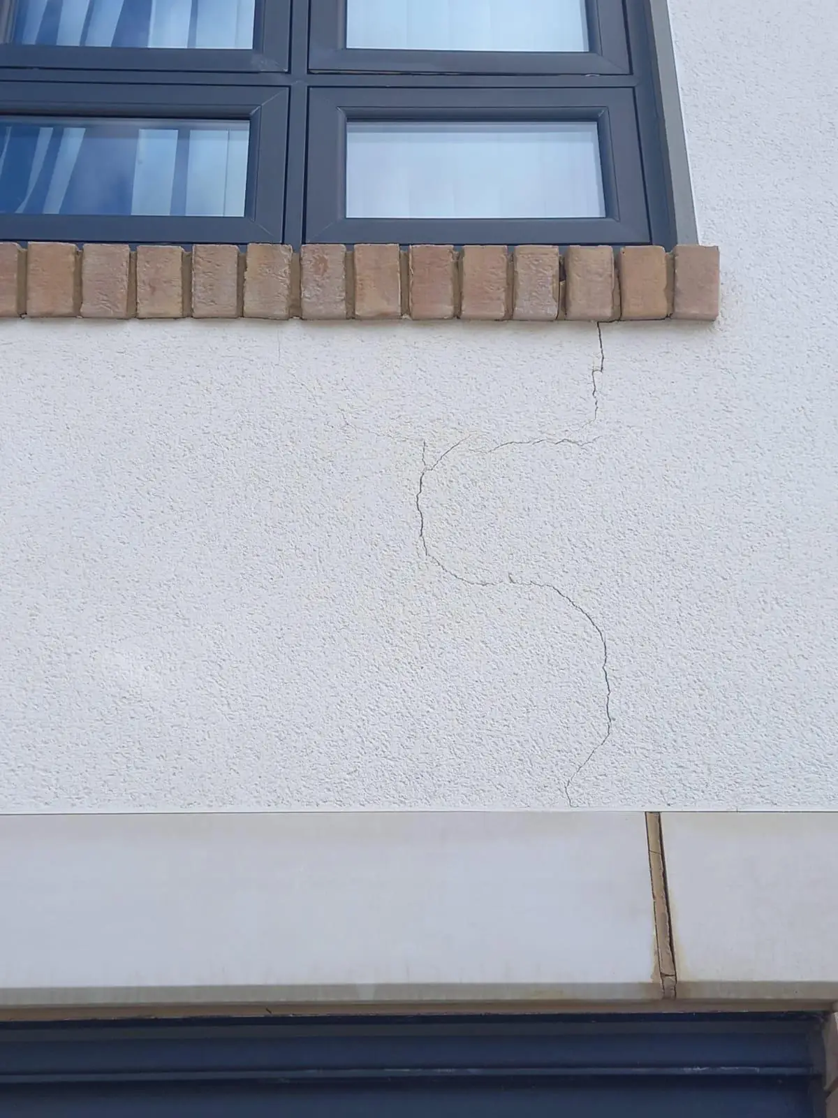 Crack running down through white render below a brick sill course
