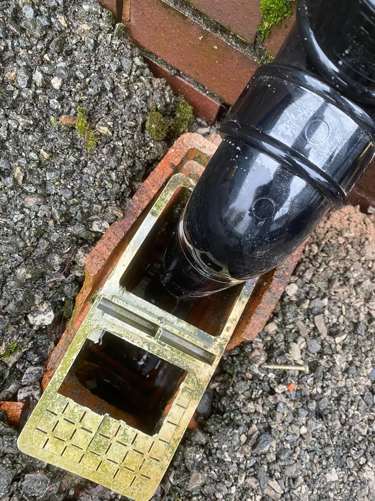 New black uPVC downpipe discharging into a yard gully at the foot of an industrial unit wall