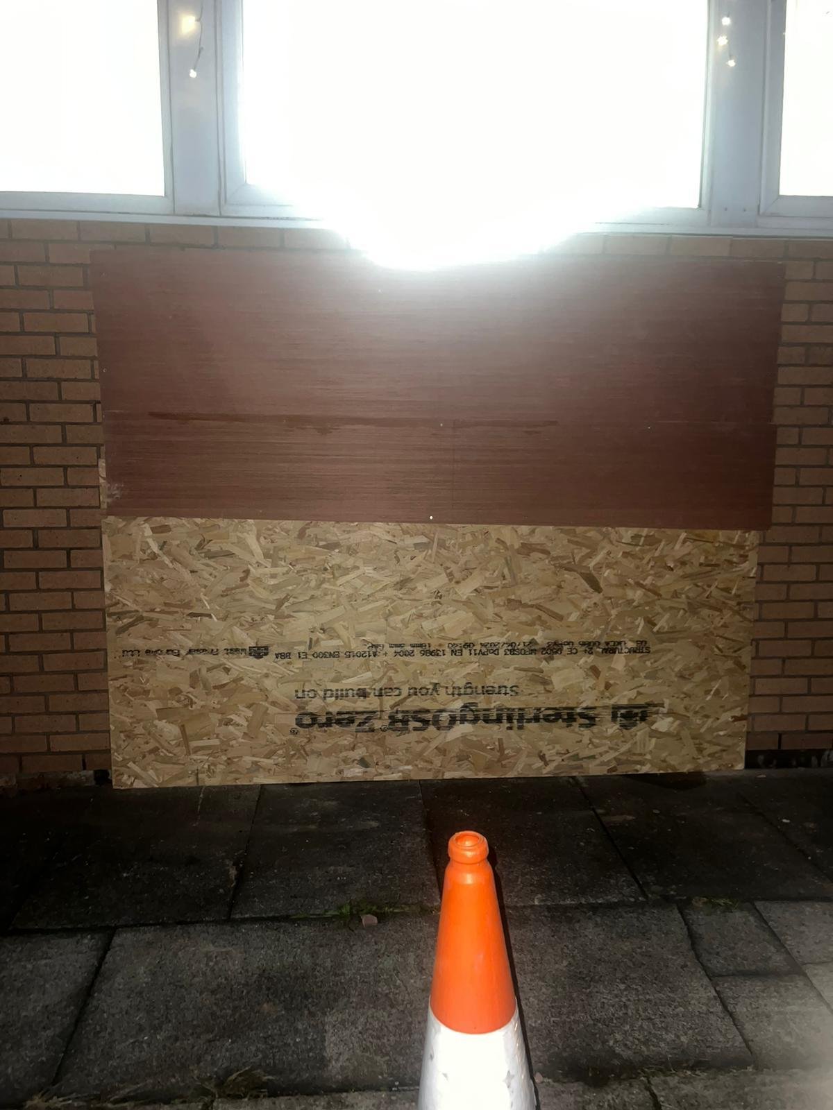 Vehicle impact opening in a brick wall boarded up at night with OSB and plywood sheets