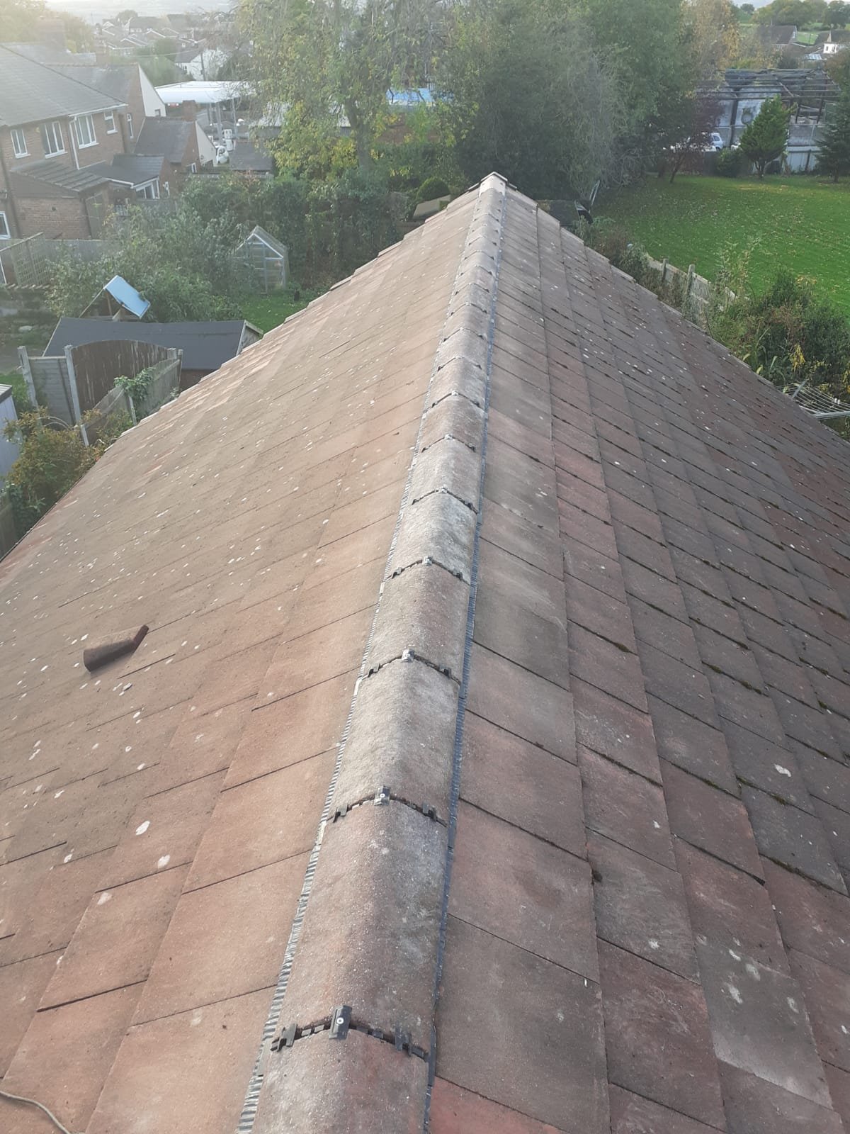 Ridge tiles refitted along a tiled roof and held with mechanical fixings, with the edge of the ventilated roll showing beneath them