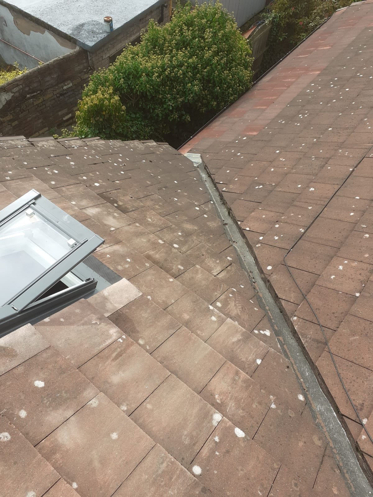 Tiled roof slope with a roof window and an abutment, the tile covering complete and even across the slope