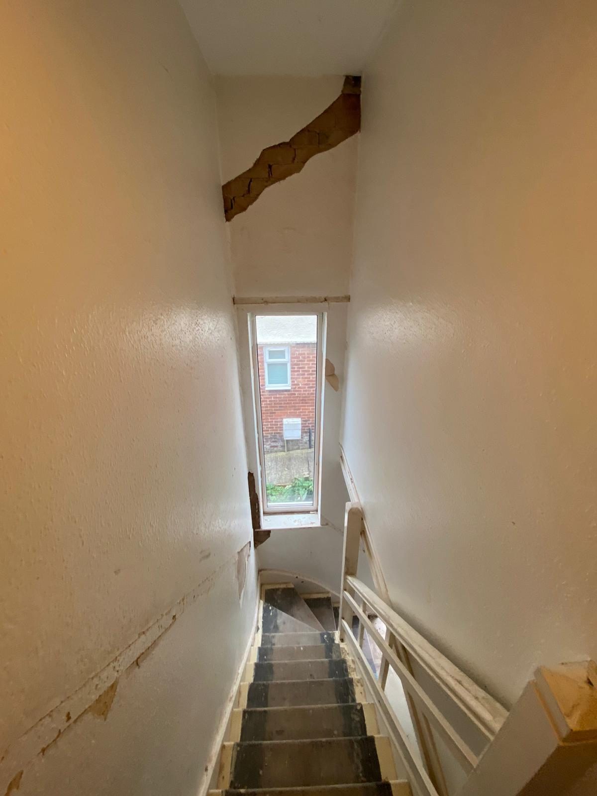 Large diagonal crack running through the plaster of a stairwell wall above a window