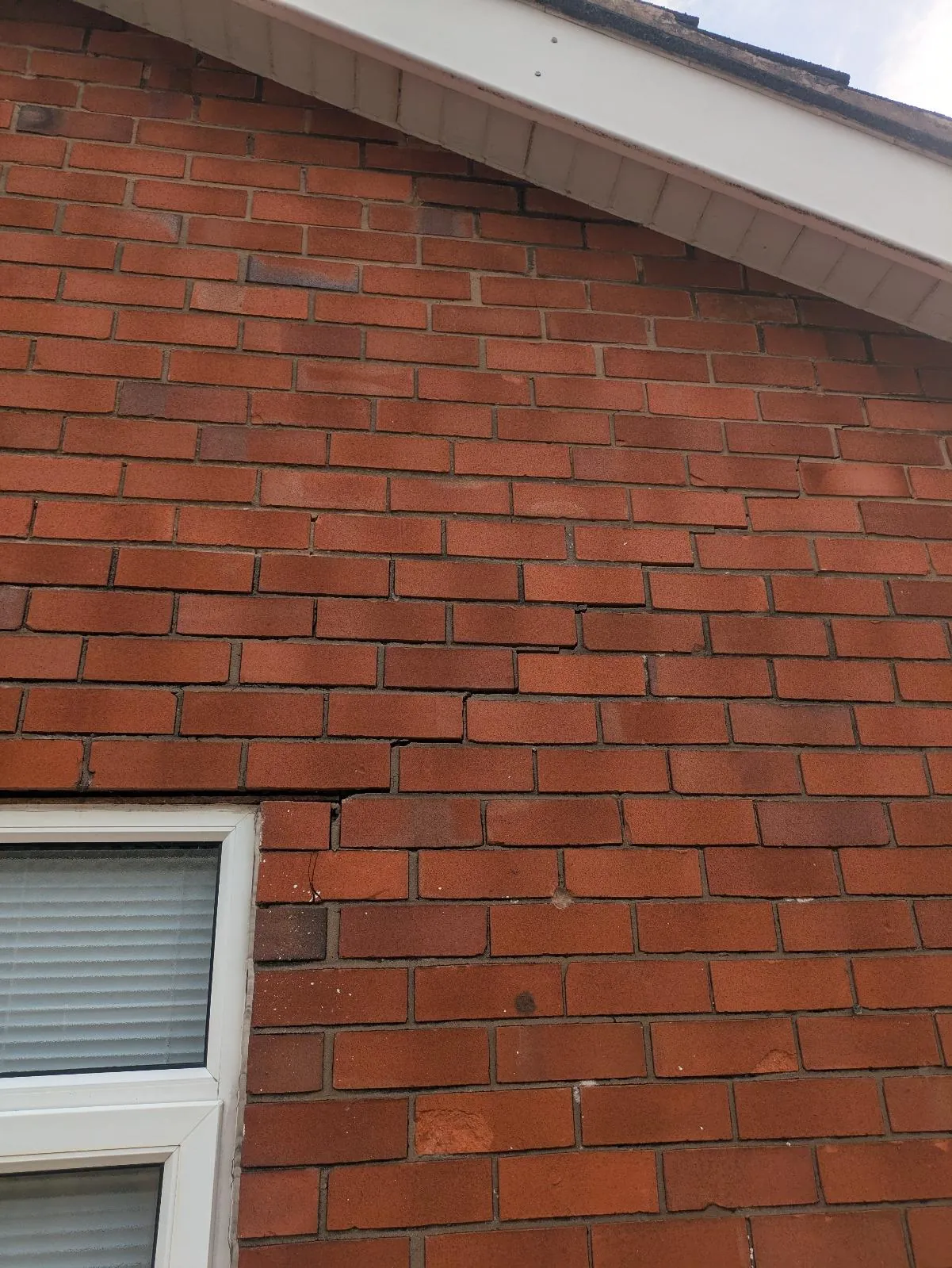 Stepped crack running up through the mortar joints of a brick gable from the top corner of a window