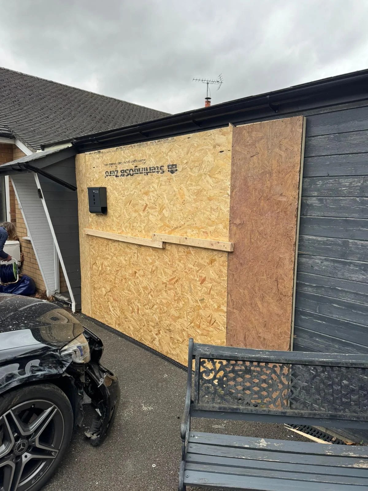 Damaged timber-clad wall of a bungalow boarded up with OSB and plywood sheets after a vehicle impact