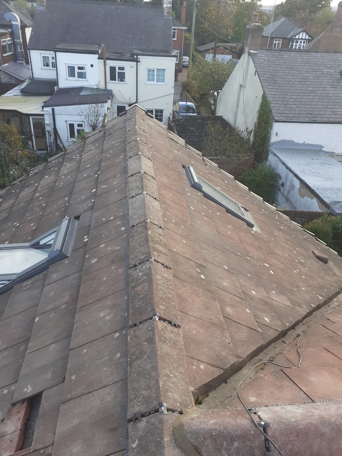 Completed ridge of a tiled bungalow roof with the ridge tiles refitted and mechanically fixed