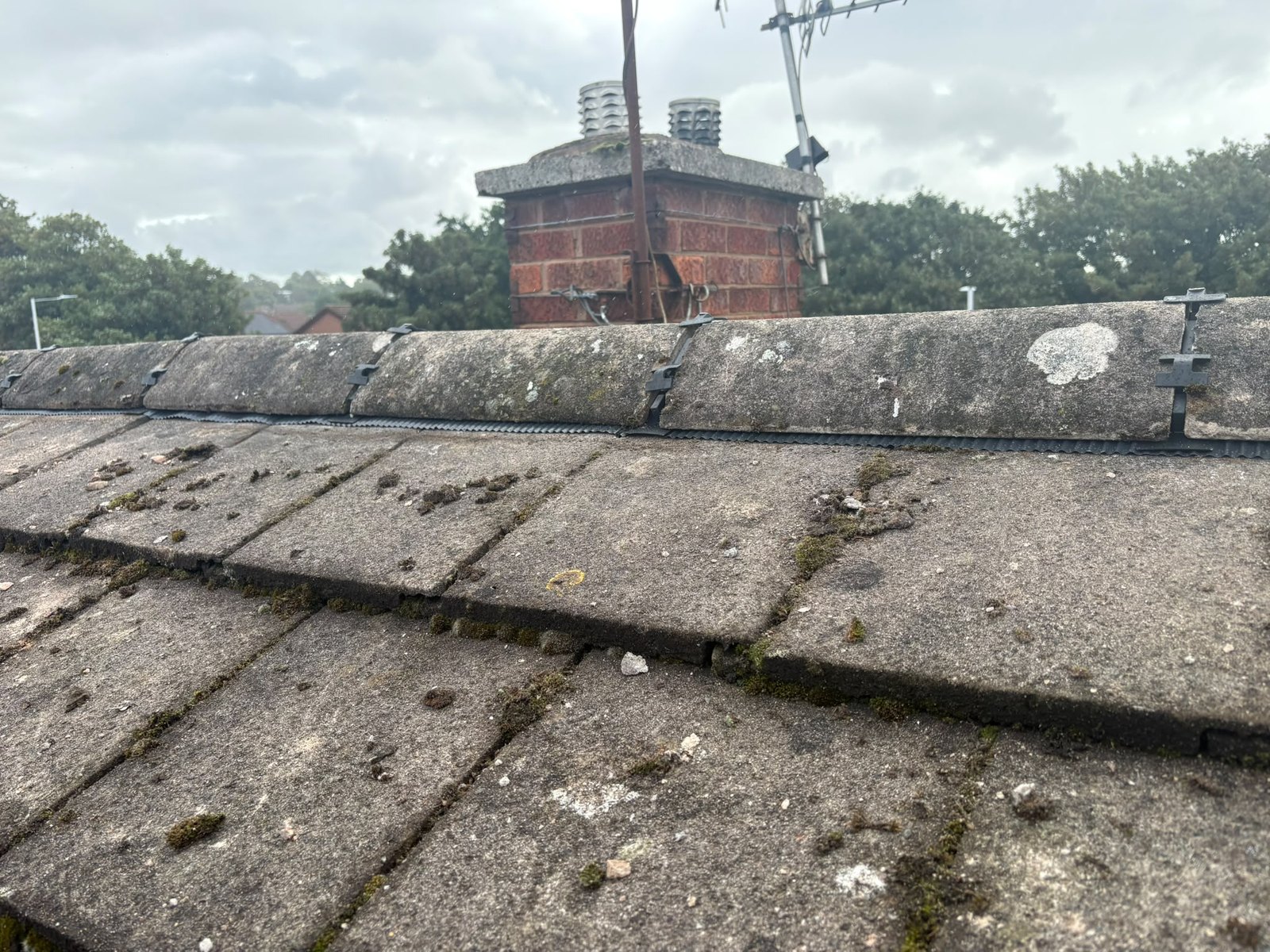 Ridge tiles refitted along the apex of a tiled roof and mechanically fixed with dry ridge fixings visible between them