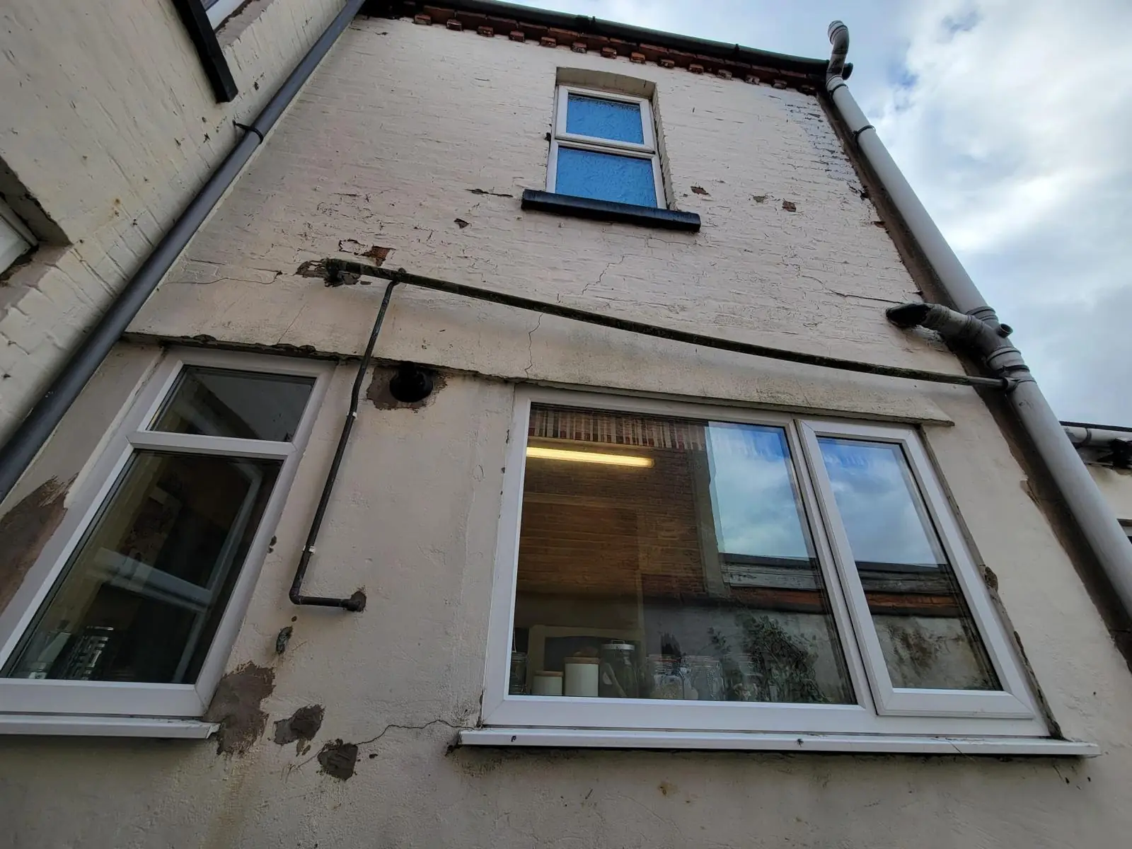 Painted brick rear wall with stepped and horizontal cracks around the ground-floor windows and old patch repairs