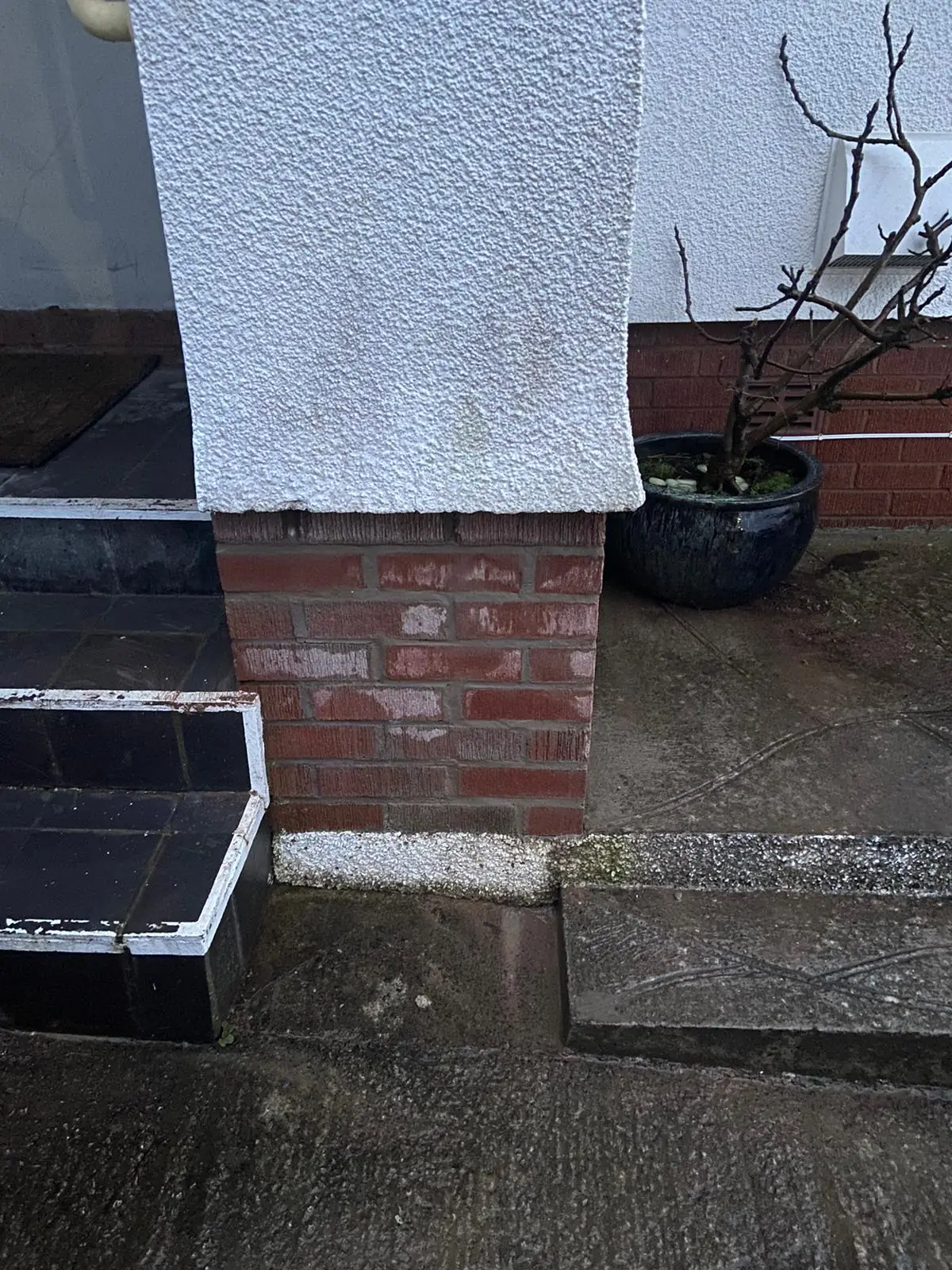 Salt deposits on the brick base of a rendered pier beside a front step