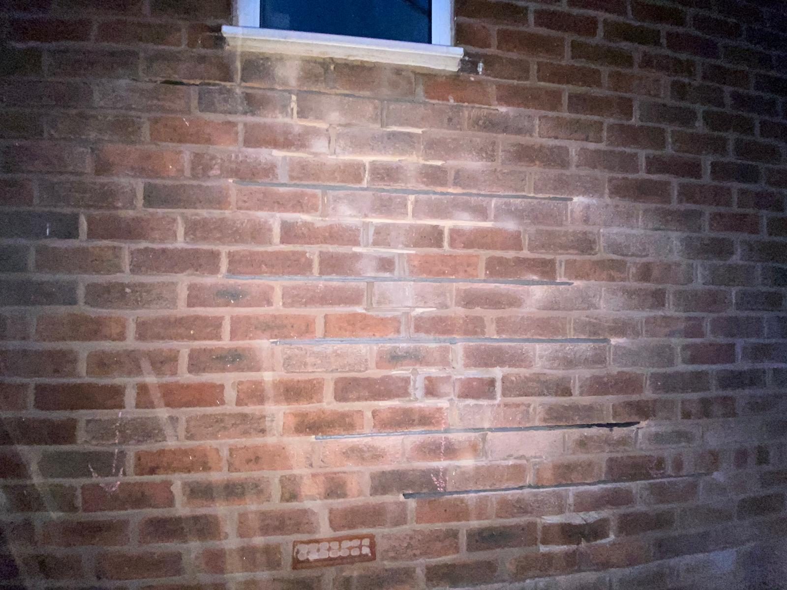 Stainless steel helical bars bedded in resin across the mortar bed joints of an external brick wall below a window