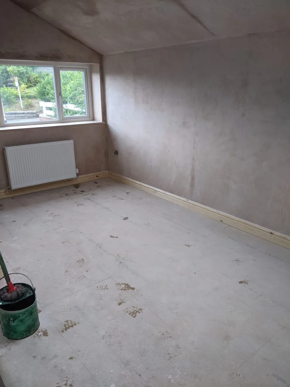 A garage conversion with the walls newly plastered and the floor prepared, ready for finishing
