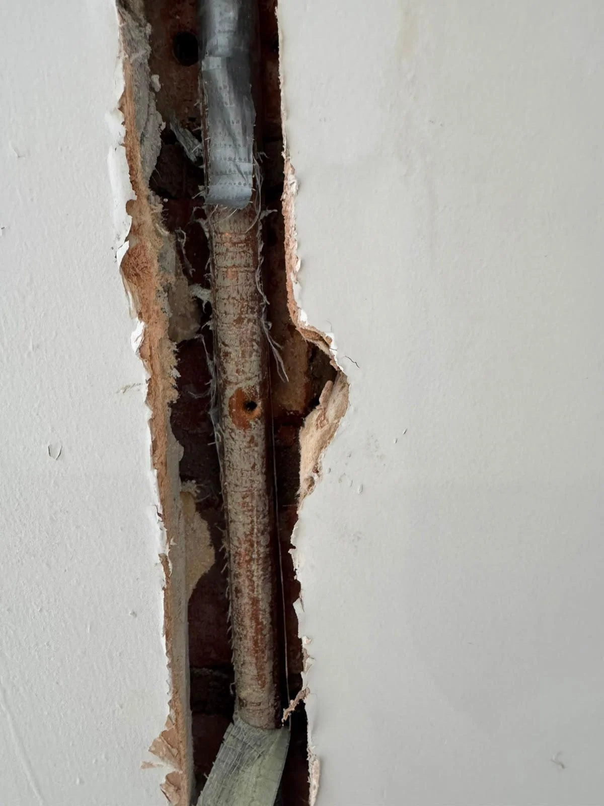 Copper pipe exposed inside a chased-out plaster wall in a Chester flat, with a nail hole through the pipe