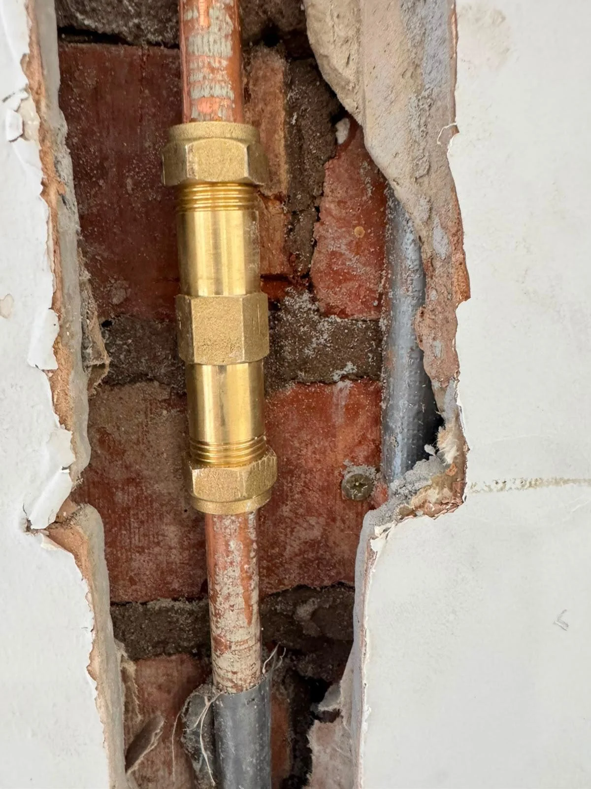New section of copper pipe fitted with brass compression fittings inside an opened-up wall