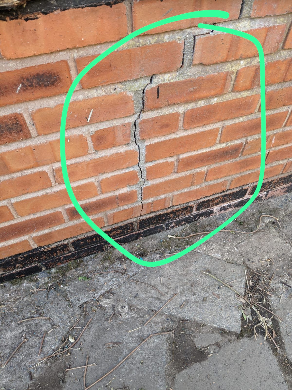 Vertical crack running down through the brickwork of an external wall above a concrete path