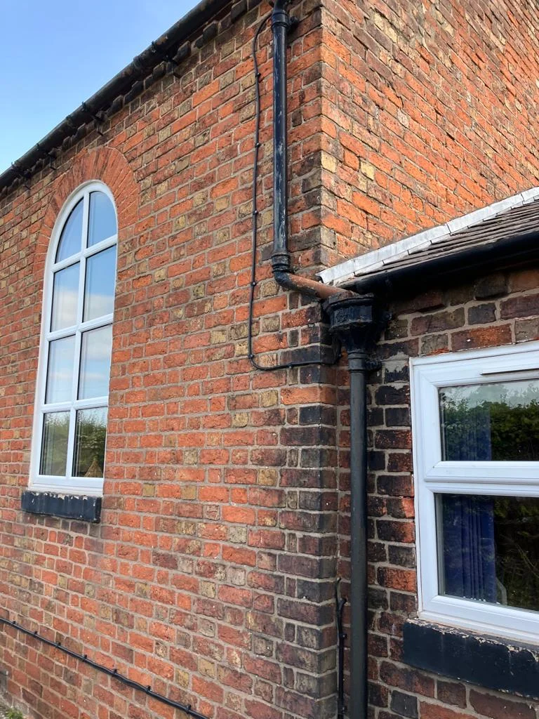 Cast-iron downpipe and hopper running down the brick gable of an older property