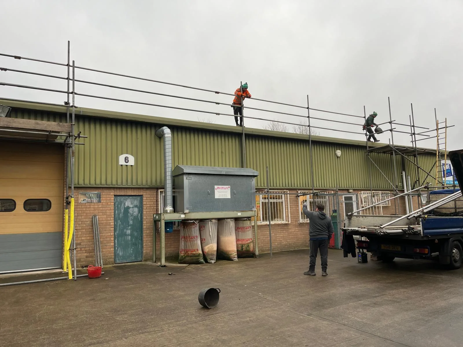 Two operatives working on the gutter line of a green-clad commercial unit from a scaffold