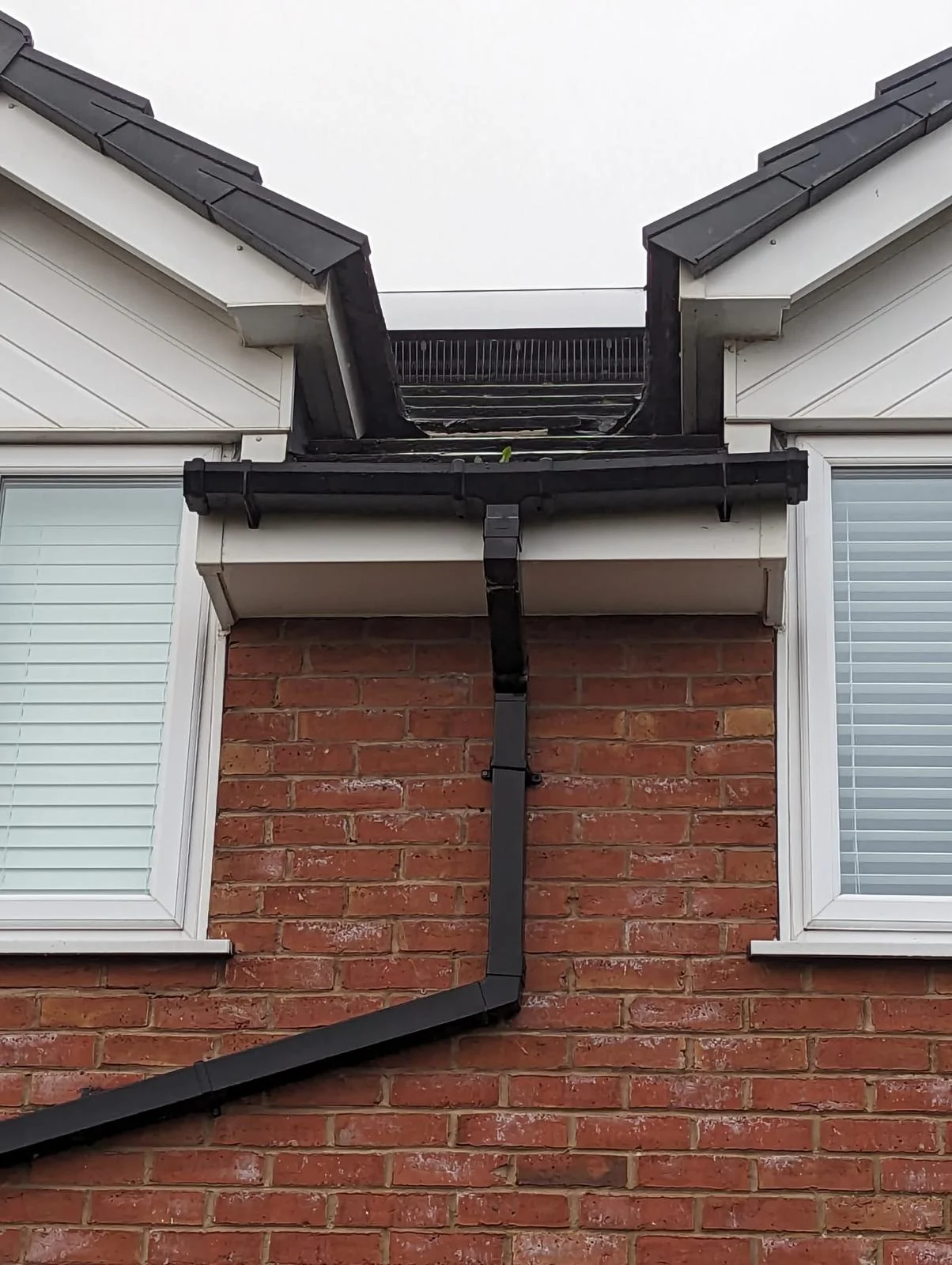 Black uPVC gutter and downpipe at the junction of two pitched roofs on a house